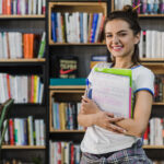 Uma aluna protagonista do seu aprendizado segura cadernos e livros em uma biblioteca escolar