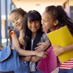 Meninas sorridentes com bom desempenho escolar, se abraçando em frente a escola