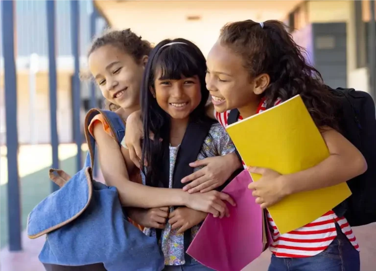 Meninas sorridentes com bom desempenho escolar, se abraçando em frente a escola