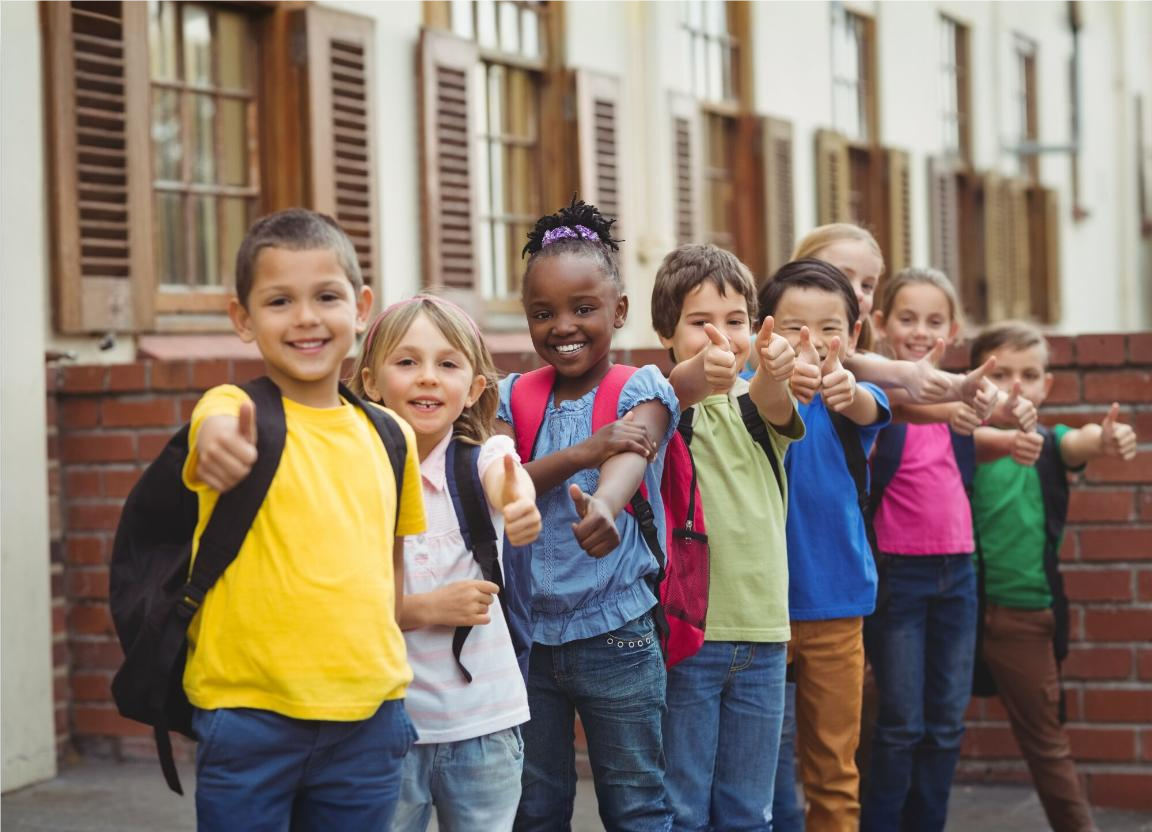 Sete crianças felizes em sua escola, posando para foto sorridentes fazendo um sinal de positivo com as mãos