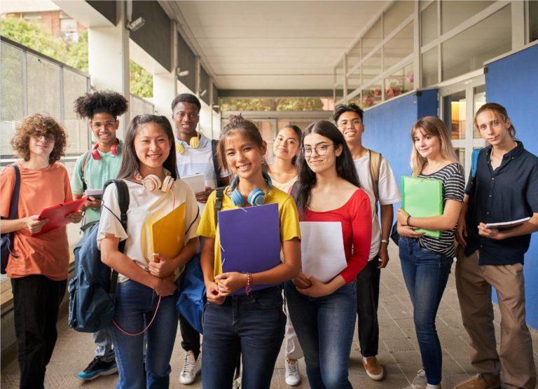 Estudantes do ensino médio sorrindo para a foto enquanto seguram seus cadernos e livros