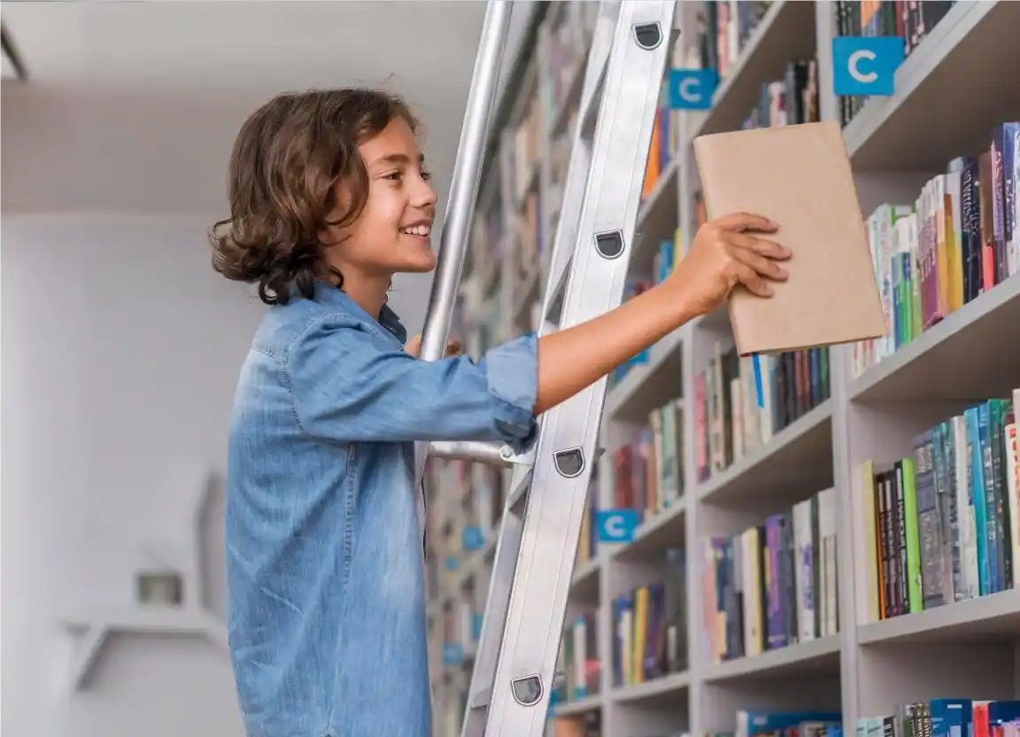 Menino sorridente pegando um livro de literatura infantil na biblioteca