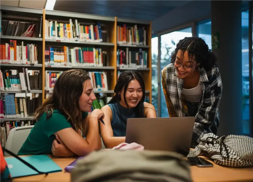 Três meninas sorridentes na biblioteca, alunos da novo Ensino Médio